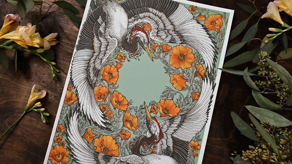 An up close photo showing the print at a diagonal from left to right. You can clearly see the center of the print. The cranes and poppies create space for an empty circle. There are fresh flowers on the table.