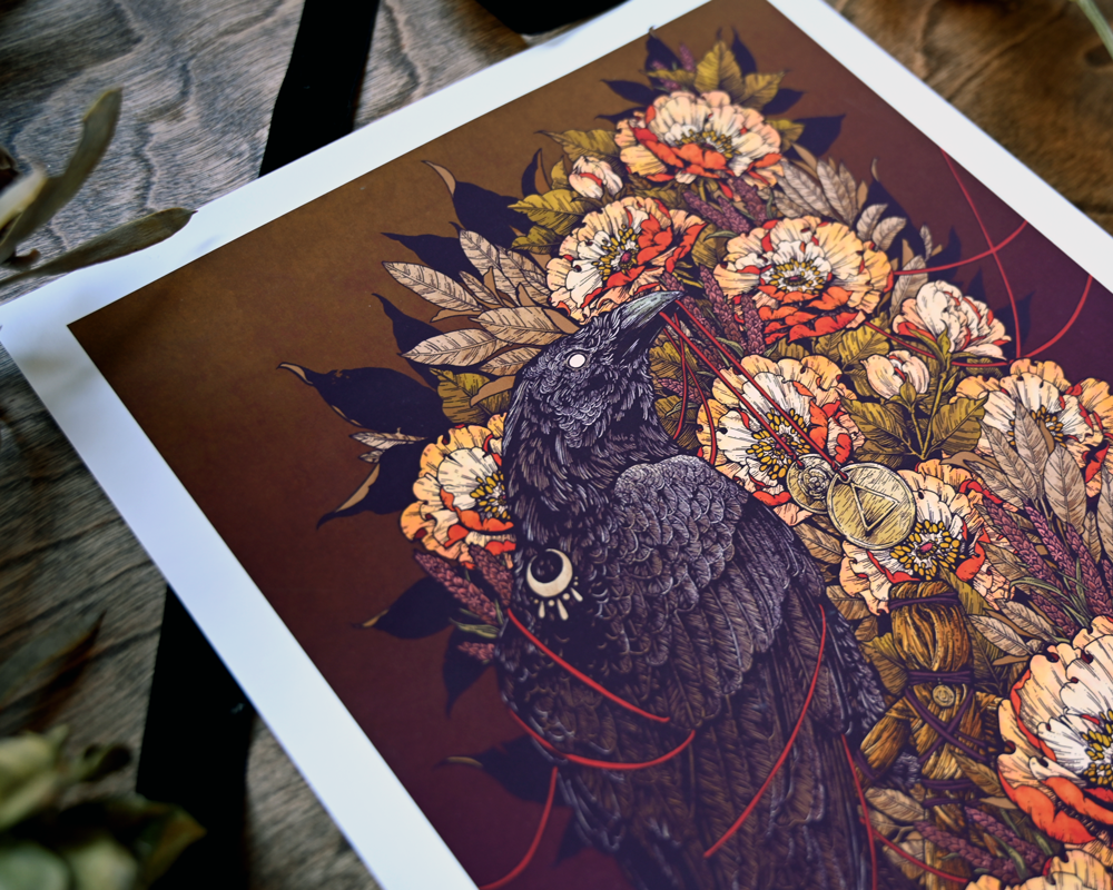 A detailed photograph showing the upper left corner of the print. You can see the crows upper body and the decorative cresent moon on its back. You can clearly see the boquette of flowers behind the crow. 