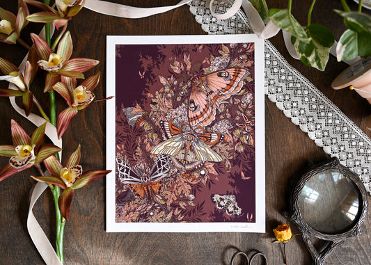A photo of a gliclee print on a wood table. You can see fake flowers, sissors, magnifying glass, and lace. The print shows strange moths above dense foliage.