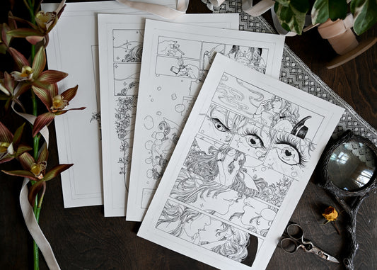 A photo showing four comic pages on a table. There is also fake orchids, ribbon, scissors, and a magnifying glass on the table. The first page of the comic shows a woman and a fairy kissing. 