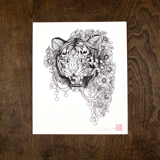 A photo of an original ink drawing on a dark wood table. The illustration is of a roaring tiger with three eyes. The tiger is surrounded by flowers with eyes in them. There are also decorative balls hanging down.
