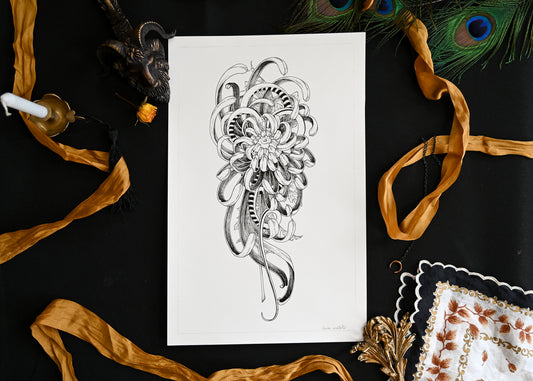 A photo of an original ink illustration sitting on a table. Around the illustration is ribbon, candle stick, a gold goat statue, peacock feather, and a hankerchief. The illustation of a mutated crysanthemum.